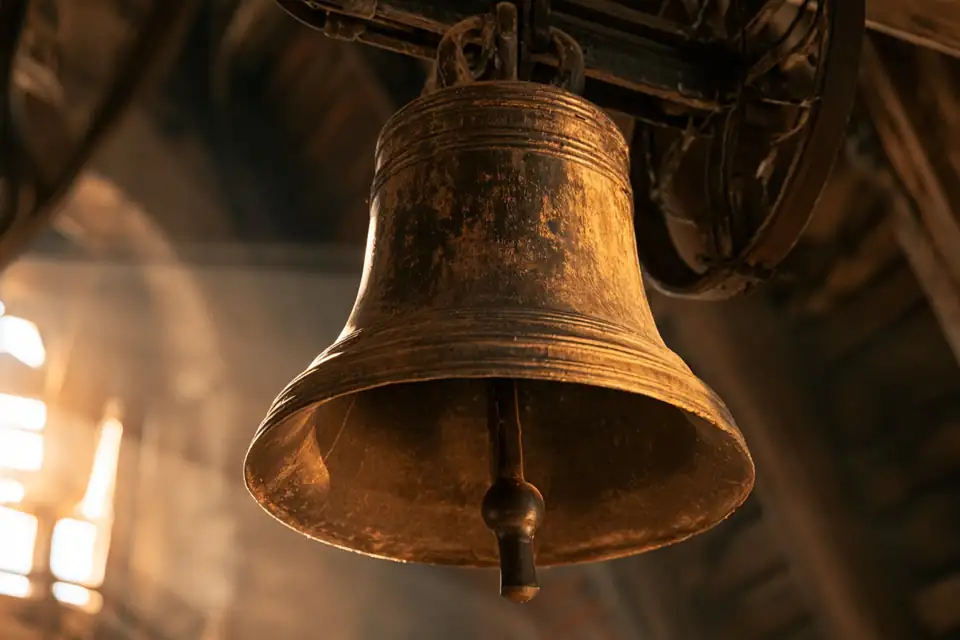 une cloche de bronze dans un clocher, la lumière qui entre par les abat-sons.