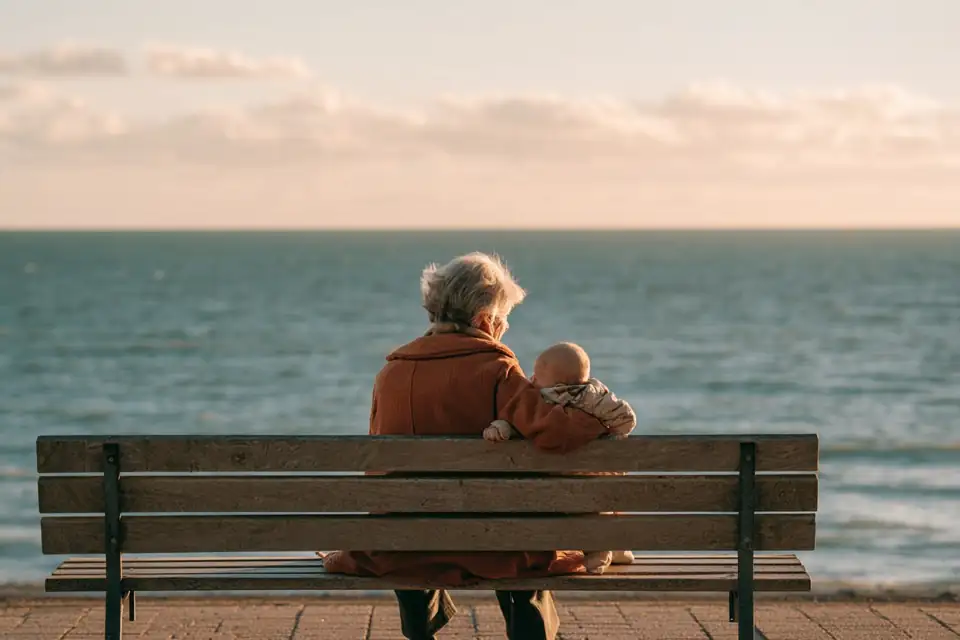 une vieille femme assise sur un banc face à la mer normande, un bébé dans les bras.