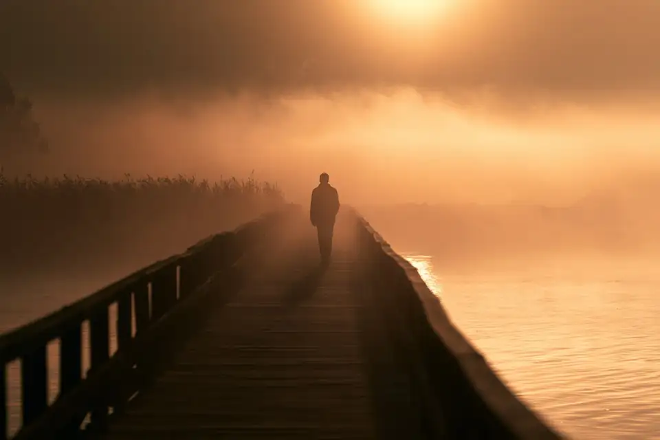 une silhouette sur un pont dans la brume, l’aube qui se lève.
