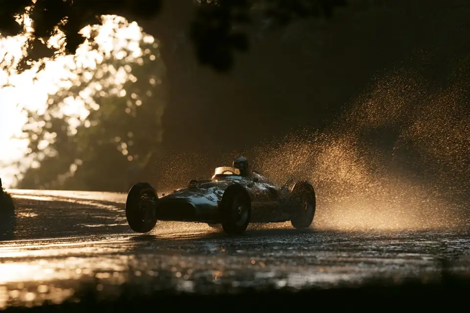 une voiture de course ancienne s’engageant dans un virage sous la pluie, une trouée de lumière devant elle.