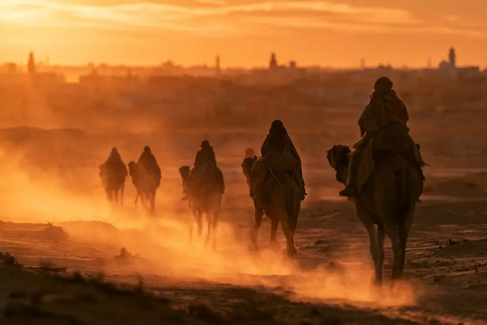 une caravane de chameaux traversant un village du désert au coucher du soleil.