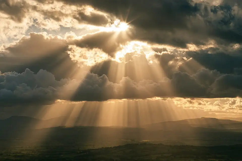 un soleil éclatant qui perce derrière une masse de nuages gris au-dessus d’une vallée.