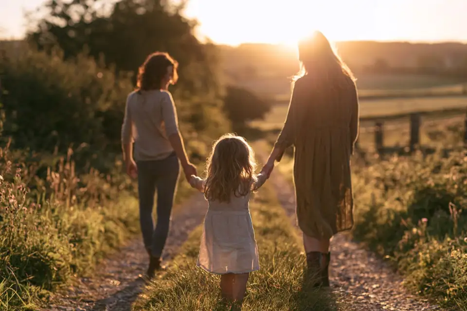 une petite fille tenant la main de deux femmes sur un chemin de campagne.