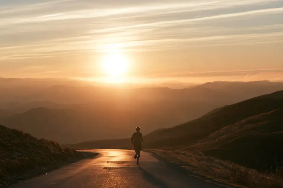 un homme qui court seul sur une route de montagne au lever du soleil.