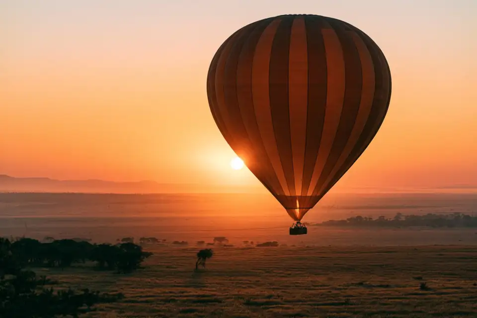 une montgolfière qui décolle au lever du soleil au-dessus d’un champ.