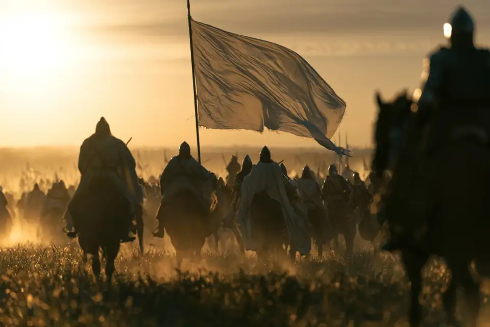 une bannière blanche flottant au-dessus de cavaliers en marche à l’aube.