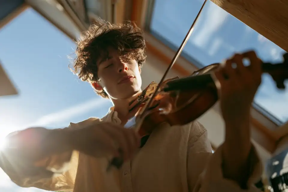 un musicien seul jouant du violon dans une mansarde froide, une bougie presque consumée.