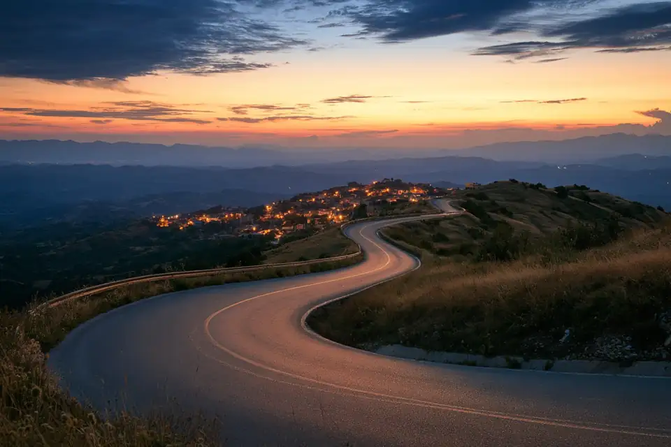 une route de montagne en lacets vue d’en haut, qui mène droit à un village éclairé.