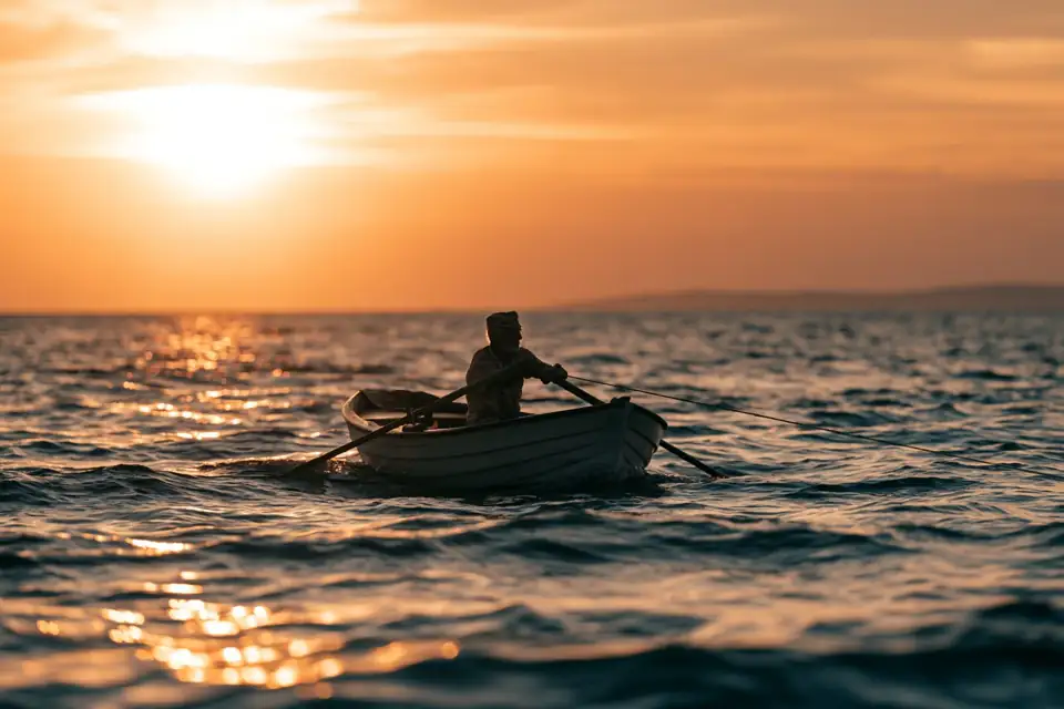 une barque au large, un vieux pêcheur tirant sur une ligne tendue, soleil couchant.